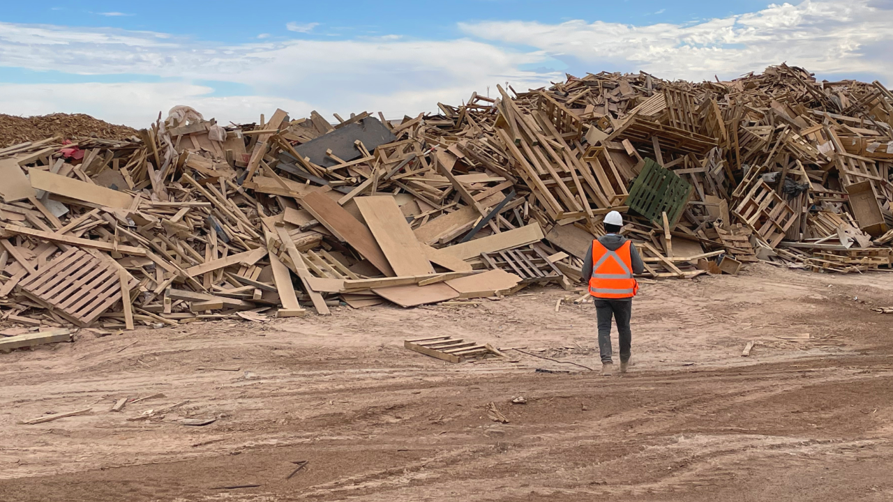 Trabajador de Bosque Ciudad frente a una acumulación de madera de descarte industrial recuperada